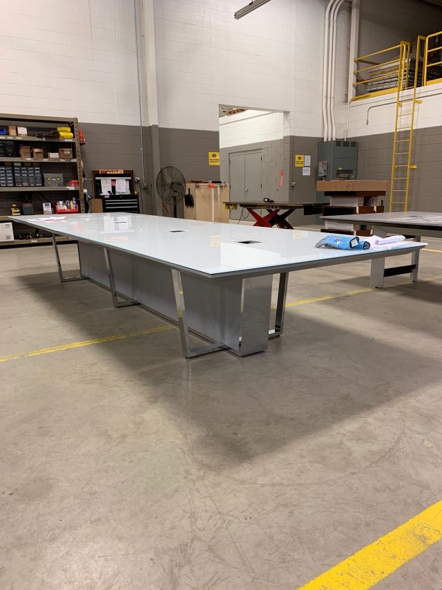 Crossbeam | Conference Table | White Backpainted Glass Top| Polished Chrome Base | Foil Painted Base Panels | Manufacturing Floor